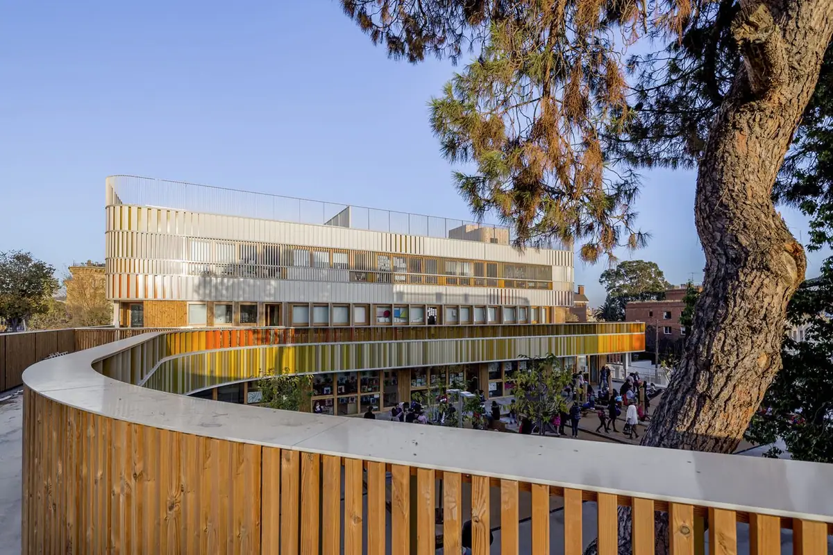 Nuevo edificio curvo con lamas de colores visto desde una pasarela con barandilla de madera y un pino