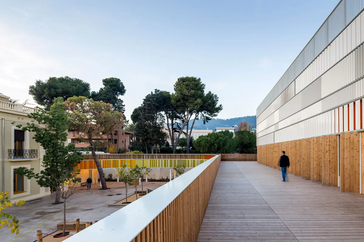 Terraza de tarima de madera junto al nuevo edificio, con la villa histórica y el patio arbolado al fondo
