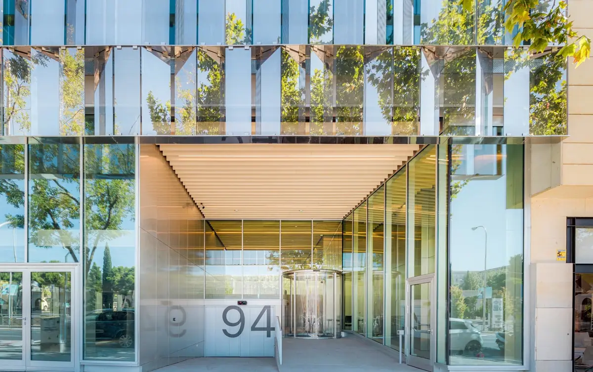 Acceso al edificio Castellana 94 bajo la piel de vidrio facetada, con el número 94 junto a la puerta giratoria