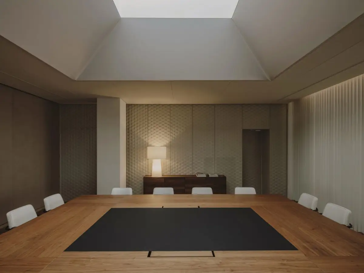 Sala de juntas con gran mesa de madera y sillas blancas bajo un lucernario abocinado