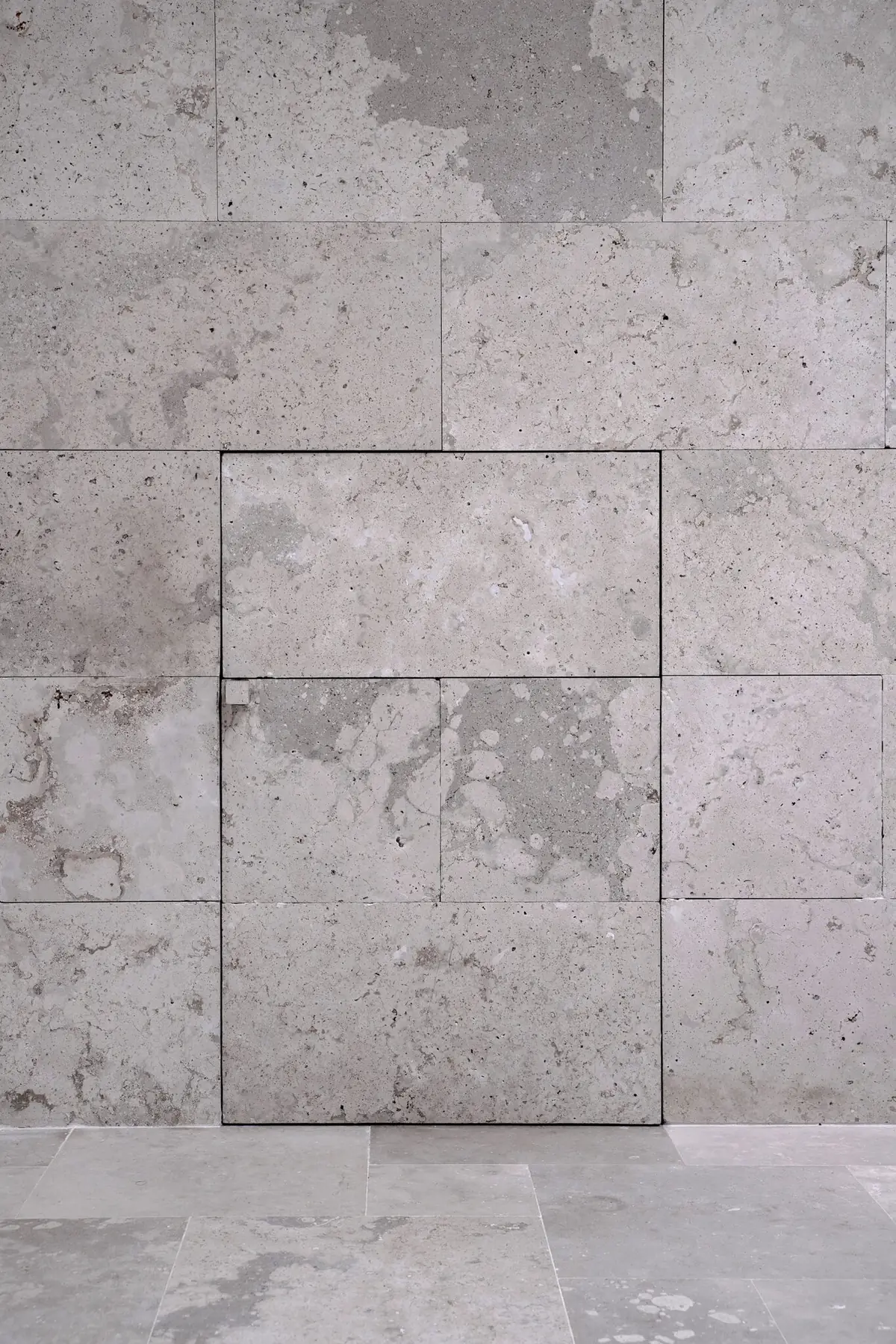 Muro aplacado con piezas de caliza gris con coqueras y una puerta enrasada en el mismo aplacado