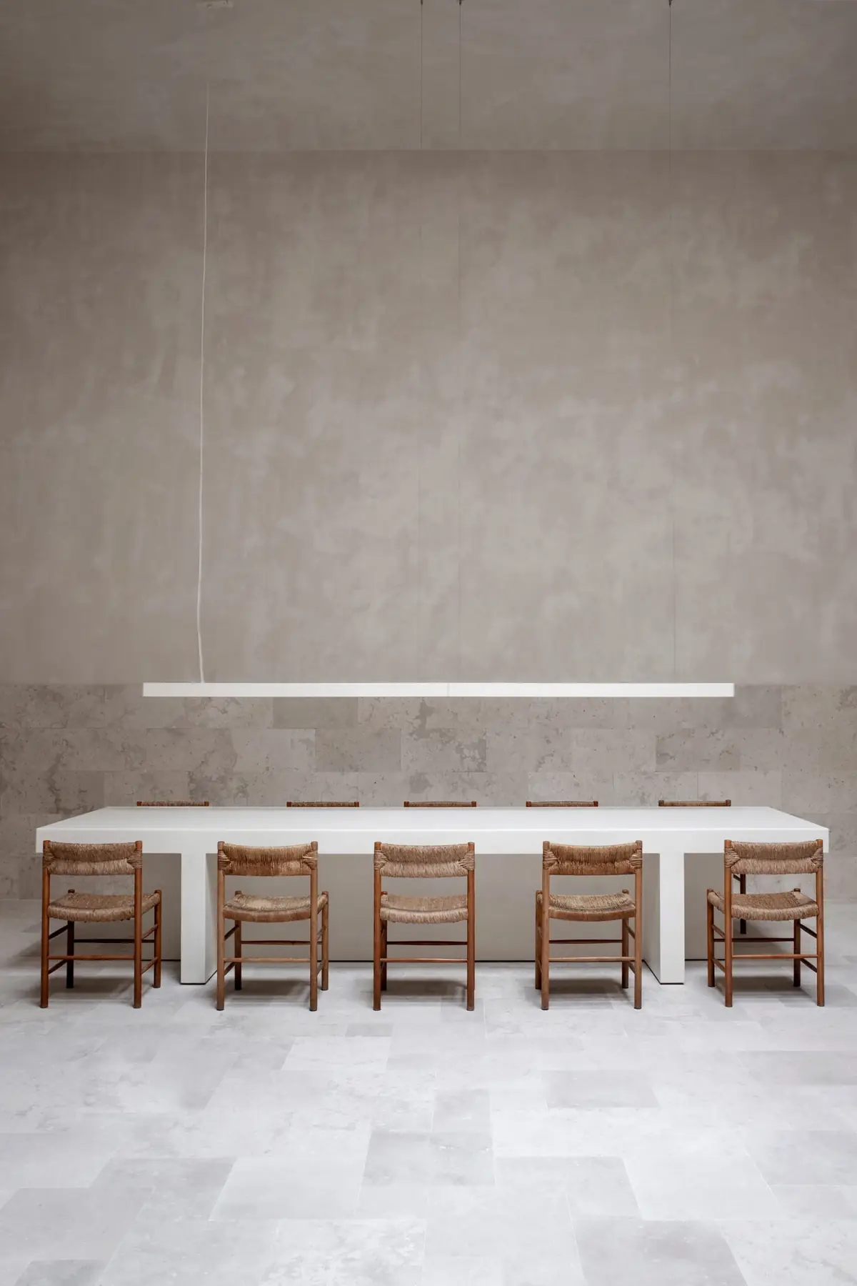 Mesa de reuniones blanca y alargada con diez sillas de madera y enea bajo una luminaria lineal