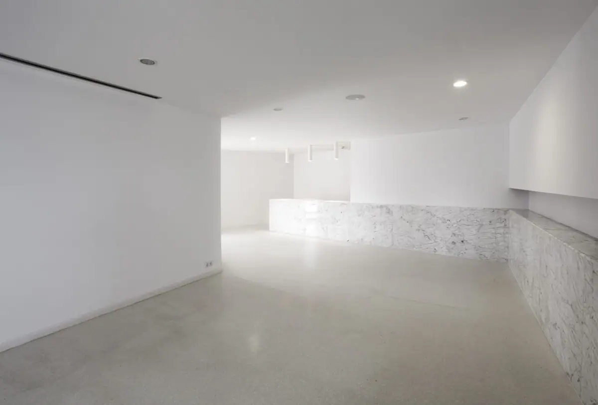 Espacio interior blanco con pavimento claro y mostrador revestido de mármol veteado