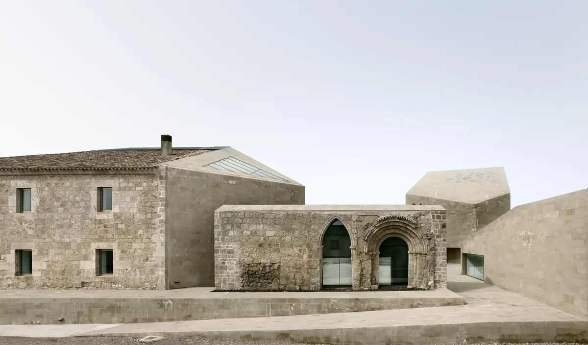 Antiguo hospital de piedra junto a un volumen que integra un arco apuntado y una portada románica