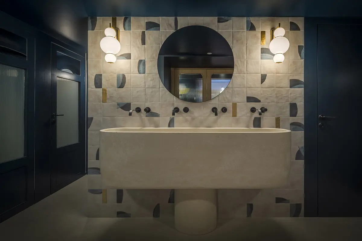 Baño con paredes azul marino, lavabo exento de piedra, espejo redondo y apliques de globo
