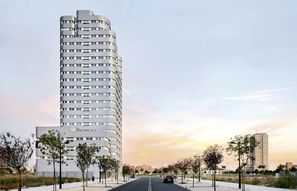 Torre Solar de Sociópolis, torre residencial curva revestida de metal claro, al atardecer con su cuerpo bajo en primer plano