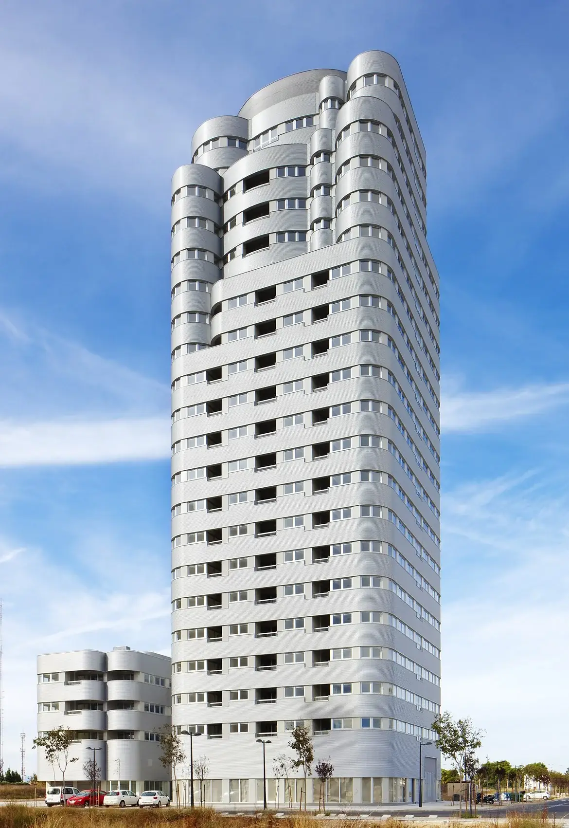 Torre Solar vista completa desde la base, con el remate curvo y fragmentado y el cuerpo bajo a la izquierda