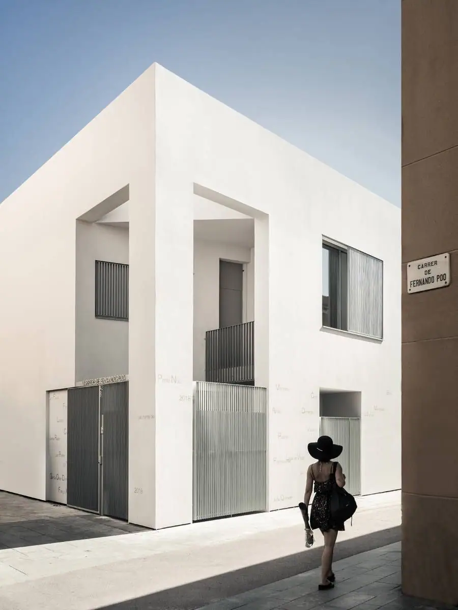 Esquina blanca con un gran vacío, puertas de lamas metálicas y la placa de la calle Fernando Poo