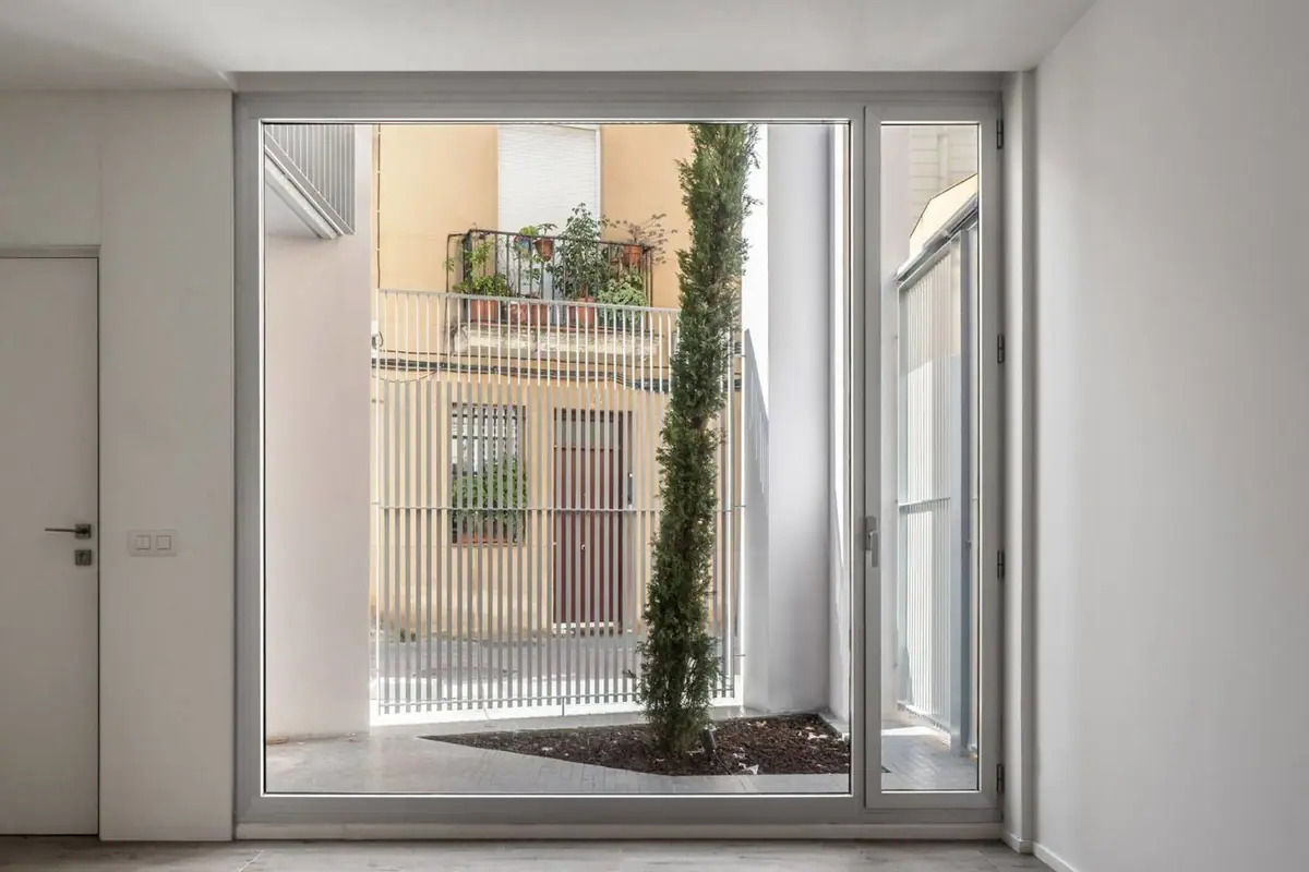 Ventanal de suelo a techo de una vivienda que da a un patio con un ciprés