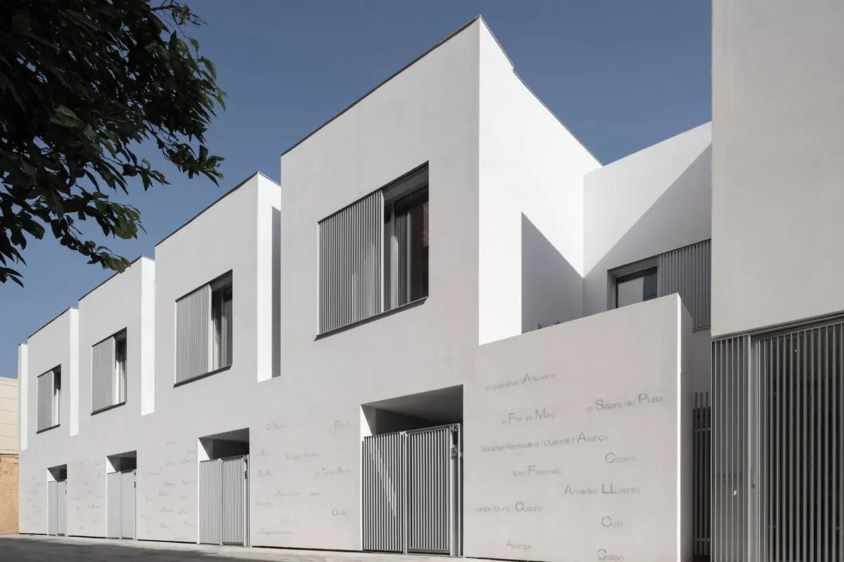 Hilera de casas blancas de dos alturas con celosías y nombres pintados en el muro de planta baja