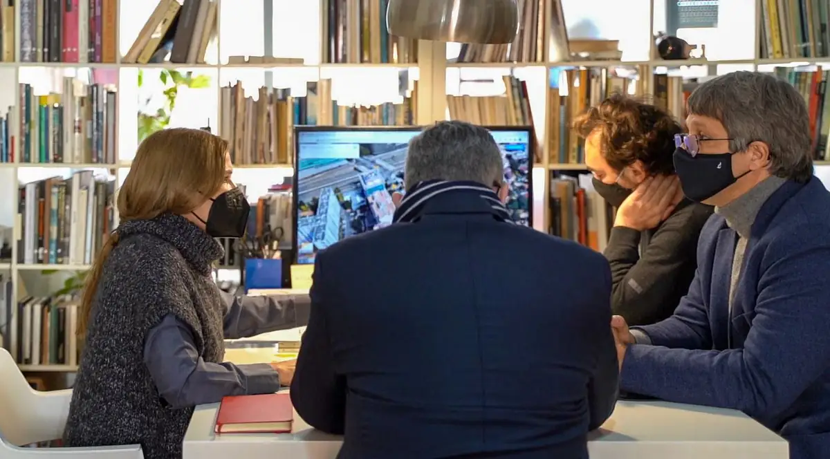 Los tres socios de Archikubik reunidos ante una pantalla con un proyecto, junto a una estantería de libros