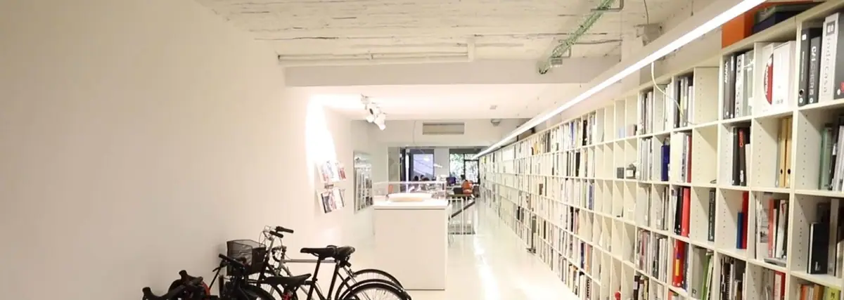 Pasillo blanco del estudio con una larga librería de revistas y archivadores a la derecha y bicicletas aparcadas a la izquierda