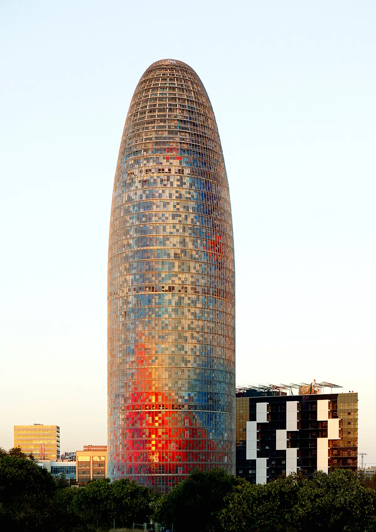 Torre Agbar al atardecer, con su fachada de lamas de colores rojos y azules sobre la vegetación