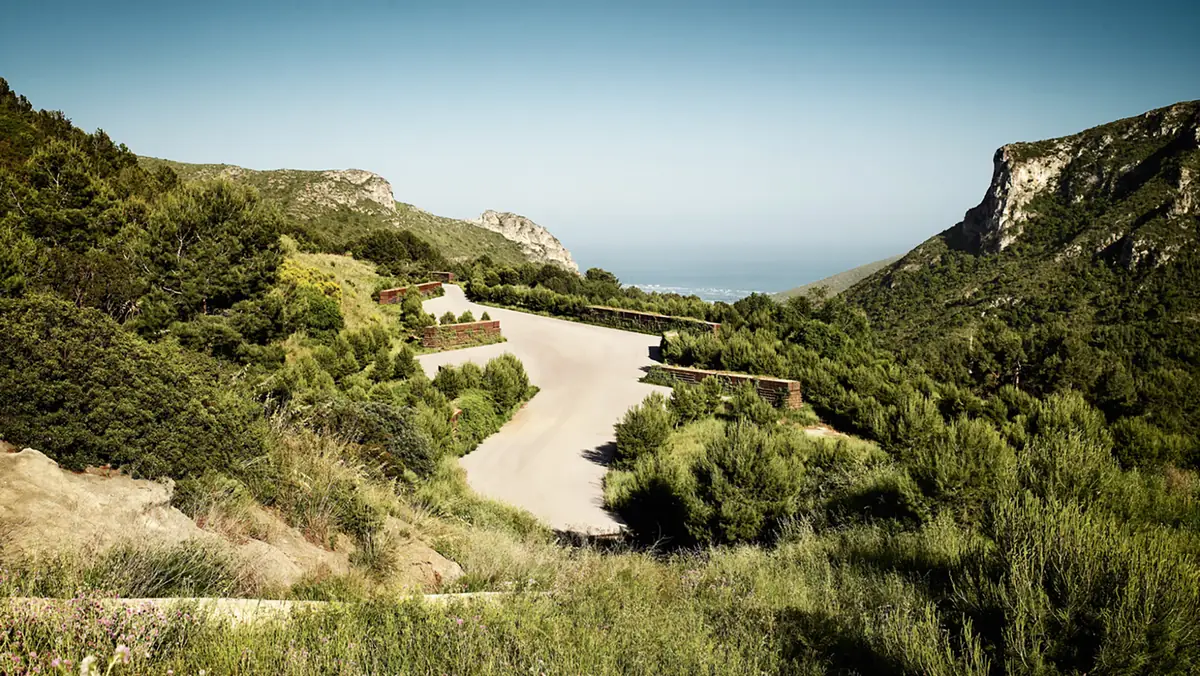 Camino entre terrazas vegetadas en la ladera restaurada del antiguo vertedero del Garraf, con el mar al fondo