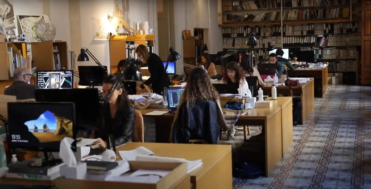 Sala de trabajo del estudio con mesas de madera, ordenadores, estanterías de archivo y suelo hidráulico