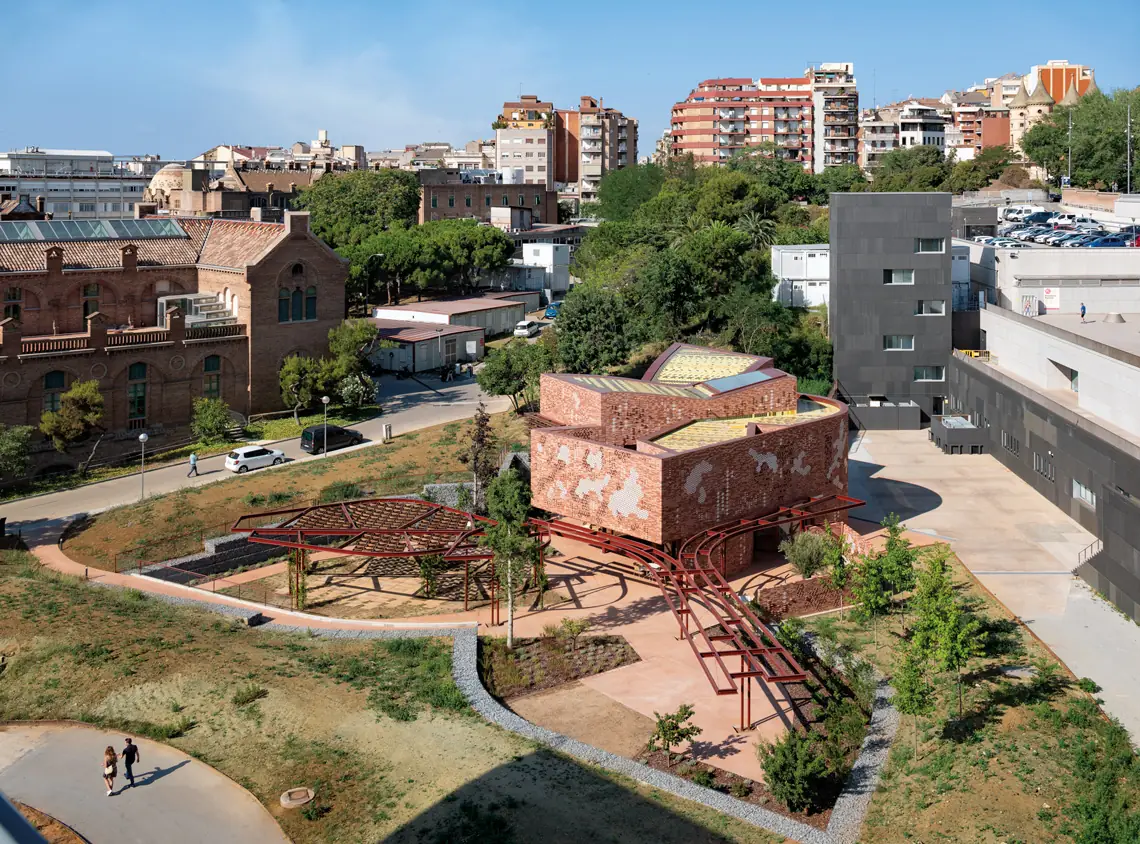 Centro Kálida Sant Pau, volumen de ladrillo con celosías cerámicas y pérgolas rojas, con los pabellones modernistas de Sant Pau al fondo
