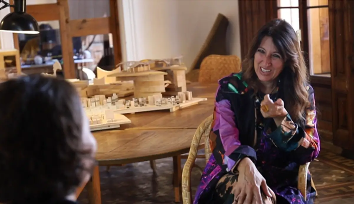 Benedetta Tagliabue conversa sentada junto a una mesa con maquetas de madera