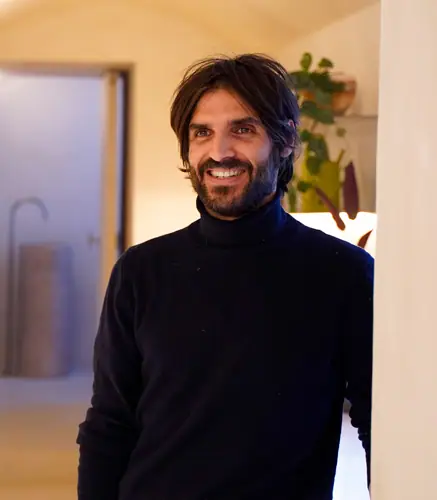 Retrato de Xabier Ortega sonriendo, con jersey negro de cuello alto, en un interior de tonos claros