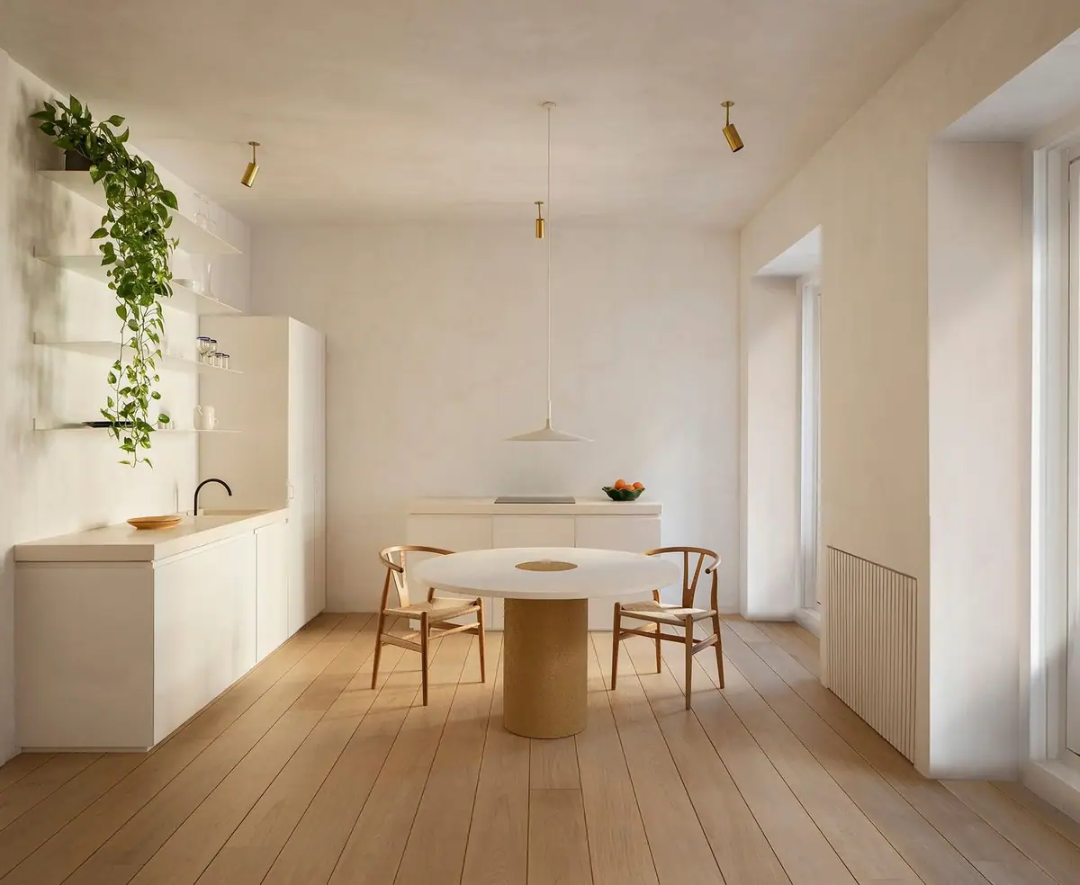 Cocina abierta de paredes blancas con mesa redonda, dos sillas de madera y suelo de tablones anchos de roble