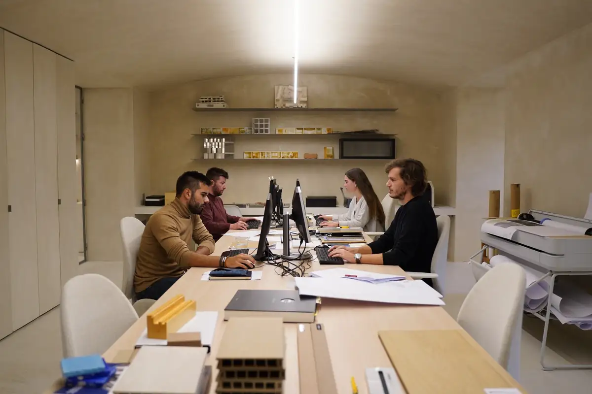 Equipo trabajando en una mesa corrida de la oficina de BETA.Ø, con muestras de materiales y maquetas en primer plano