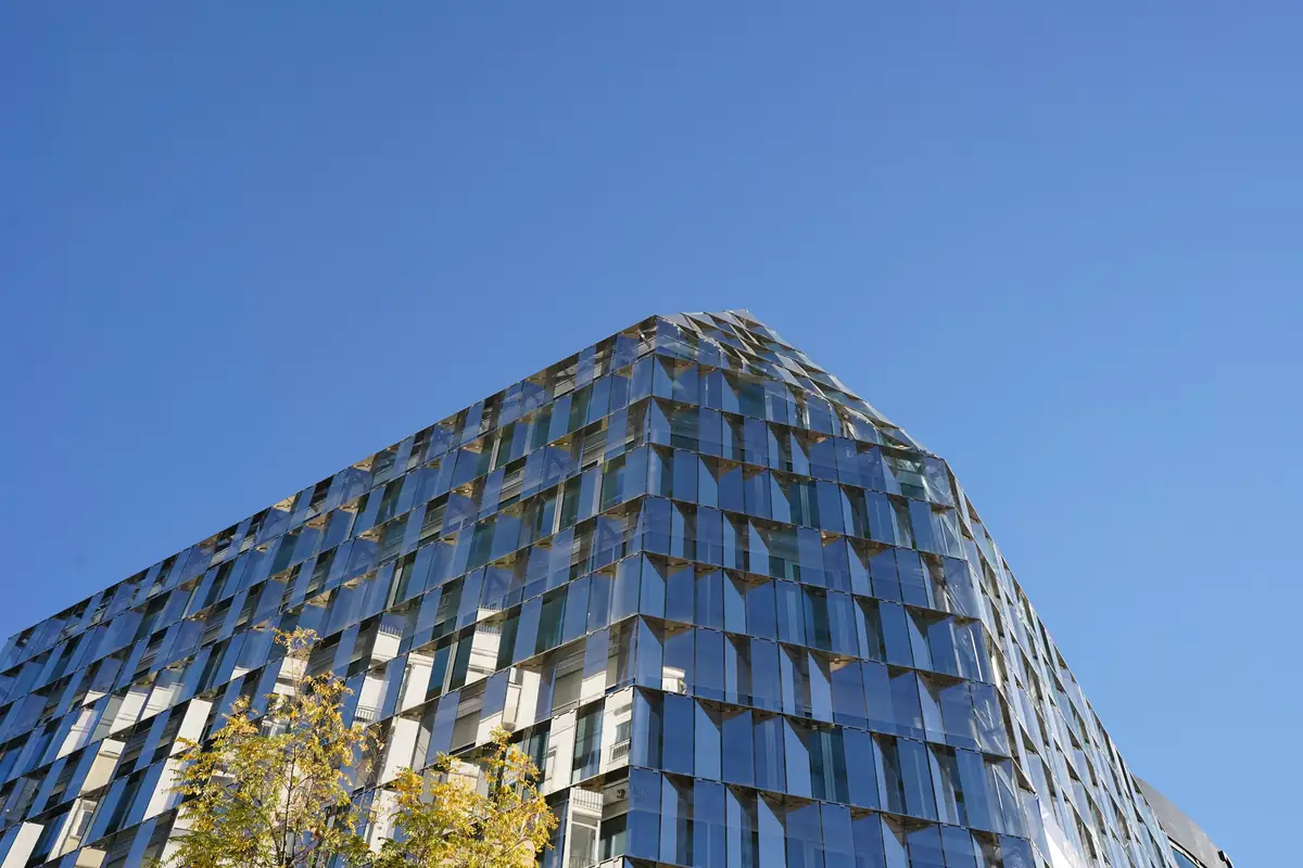 Esquina del edificio de oficinas de Paseo de la Castellana 94 con su fachada de vidrio facetada sobre el cielo azul