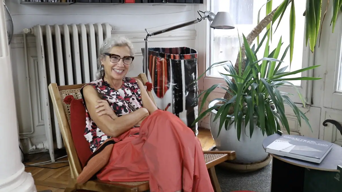 Carme Pinós sonríe sentada en una butaca junto a una planta y un radiador en su estudio