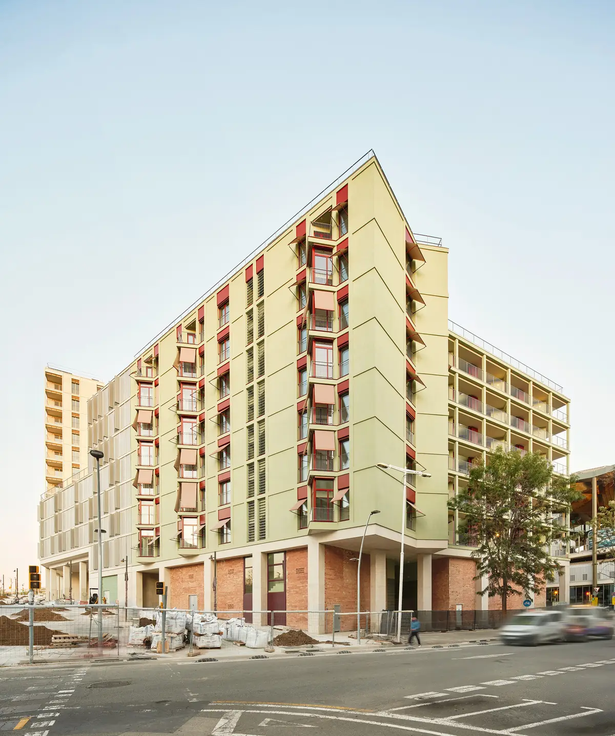 Edificio de viviendas de fachada verde clara con toldos y carpinterías rojas en una esquina de Barcelona
