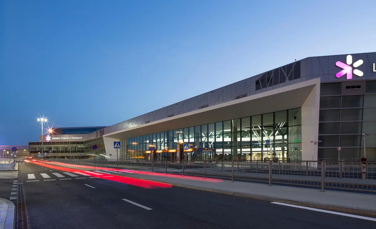 Fachada acristalada de la terminal del aeropuerto Chopin de Varsovia al anochecer, con una gran visera blanca