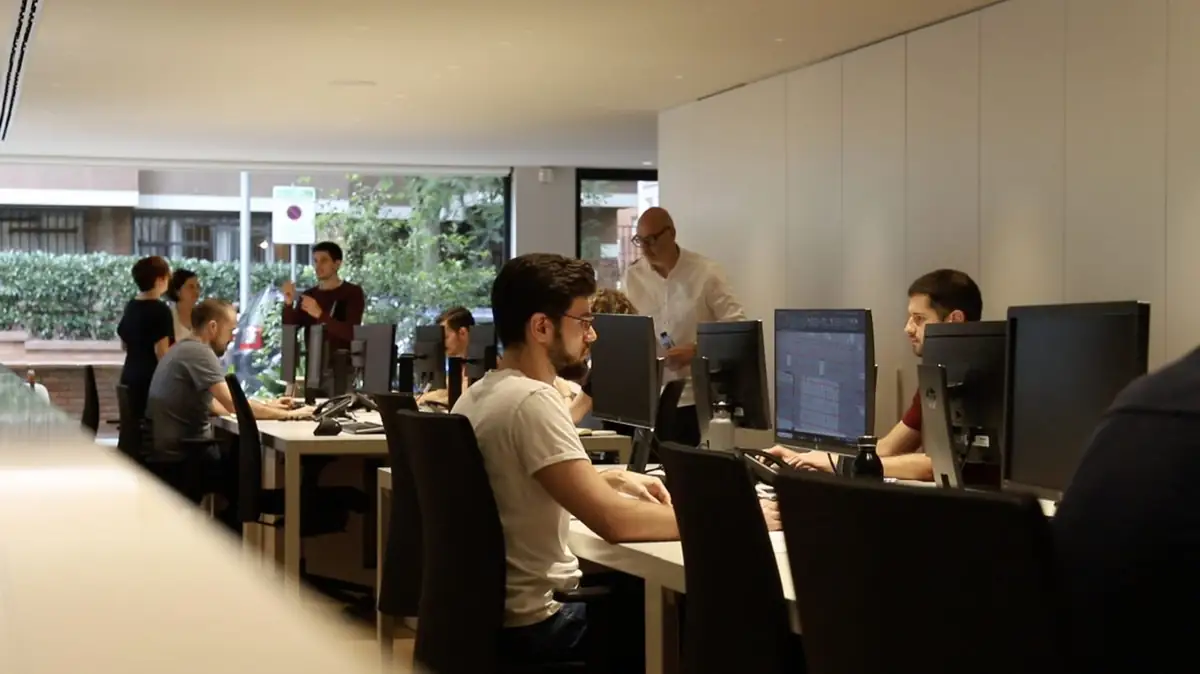 Francesc Rifé, de pie y con camisa blanca, conversa con el equipo en la sala de trabajo