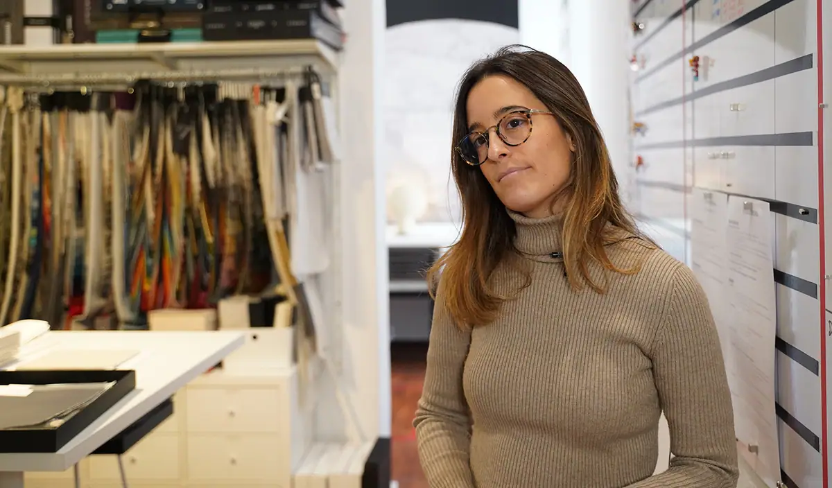 Anna Fajertag, con gafas y jersey de cuello alto, junto a un muestrario de tejidos en el estudio