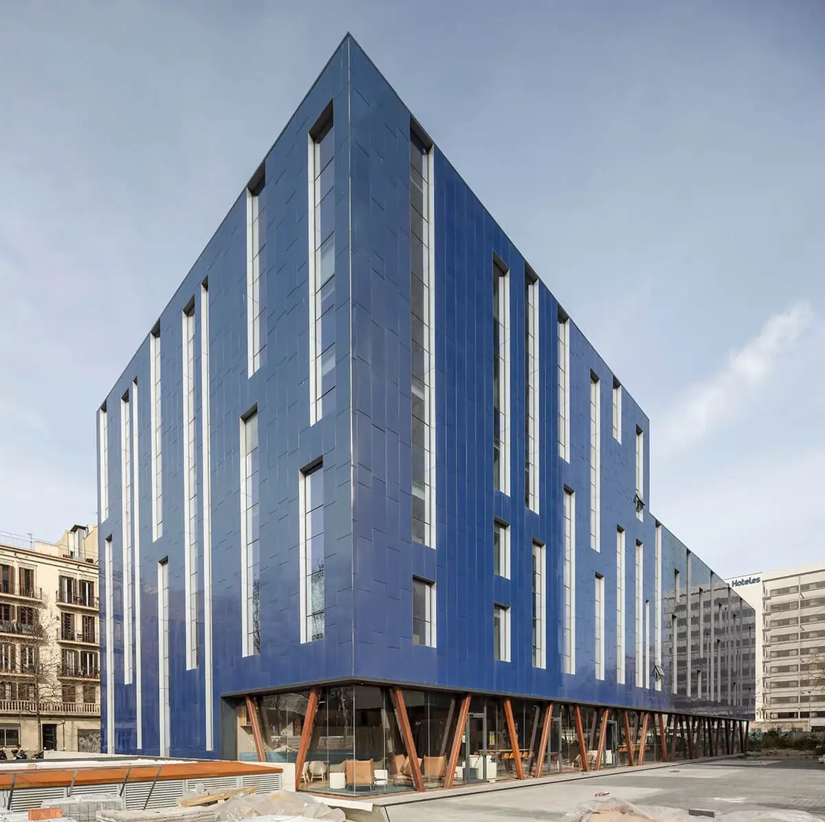 Fachada del Hotel Paxton de Barcelona, revestida con piezas verticales en tonos azules y con la planta baja acristalada sobre pilares en V