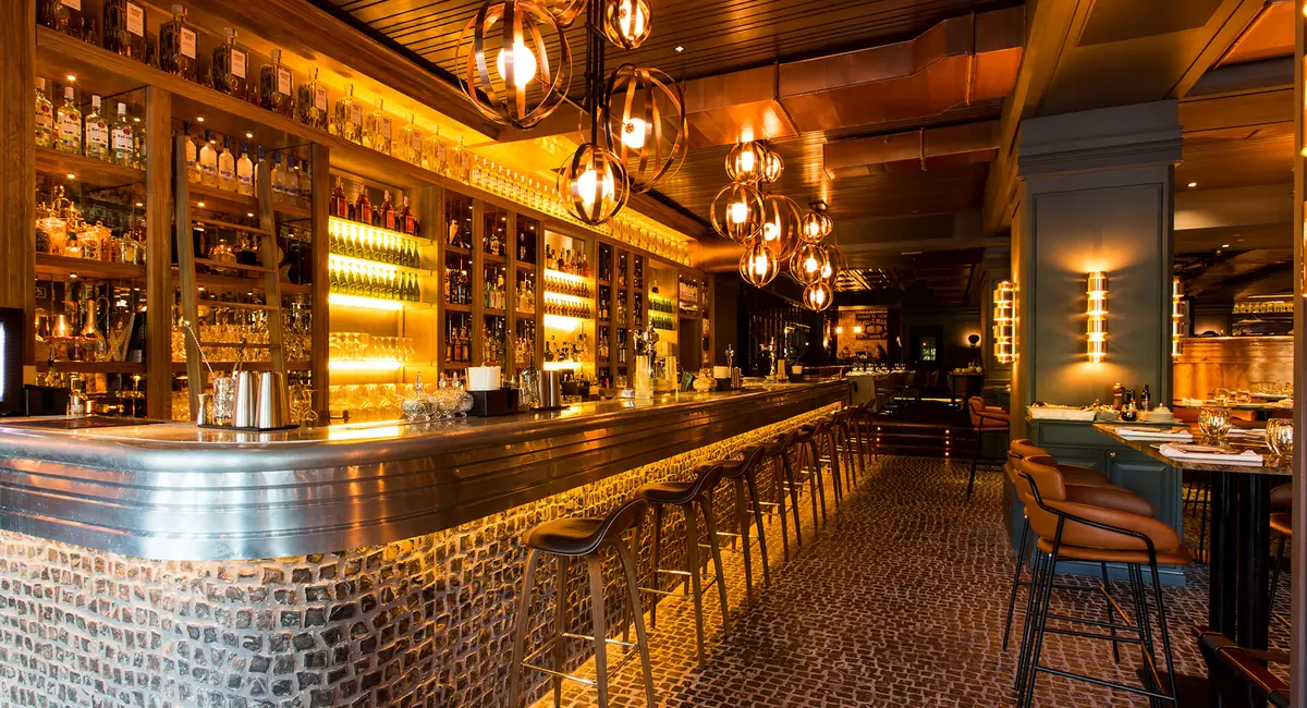 Barra del restaurante Tatel Madrid con frente de piedra, sobre de metal, botelleros iluminados y lámparas esféricas de latón