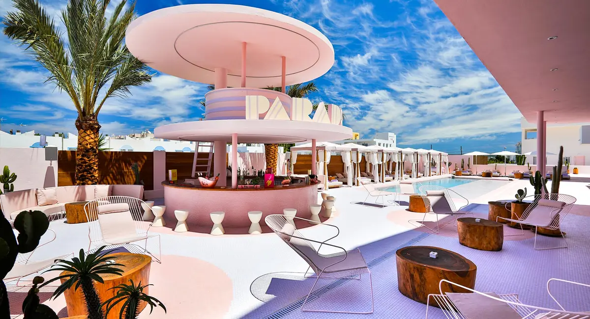 Terraza de la piscina del Paradiso Ibiza Art Hotel con barra circular rosa, palmeras, cactus y tumbonas blancas