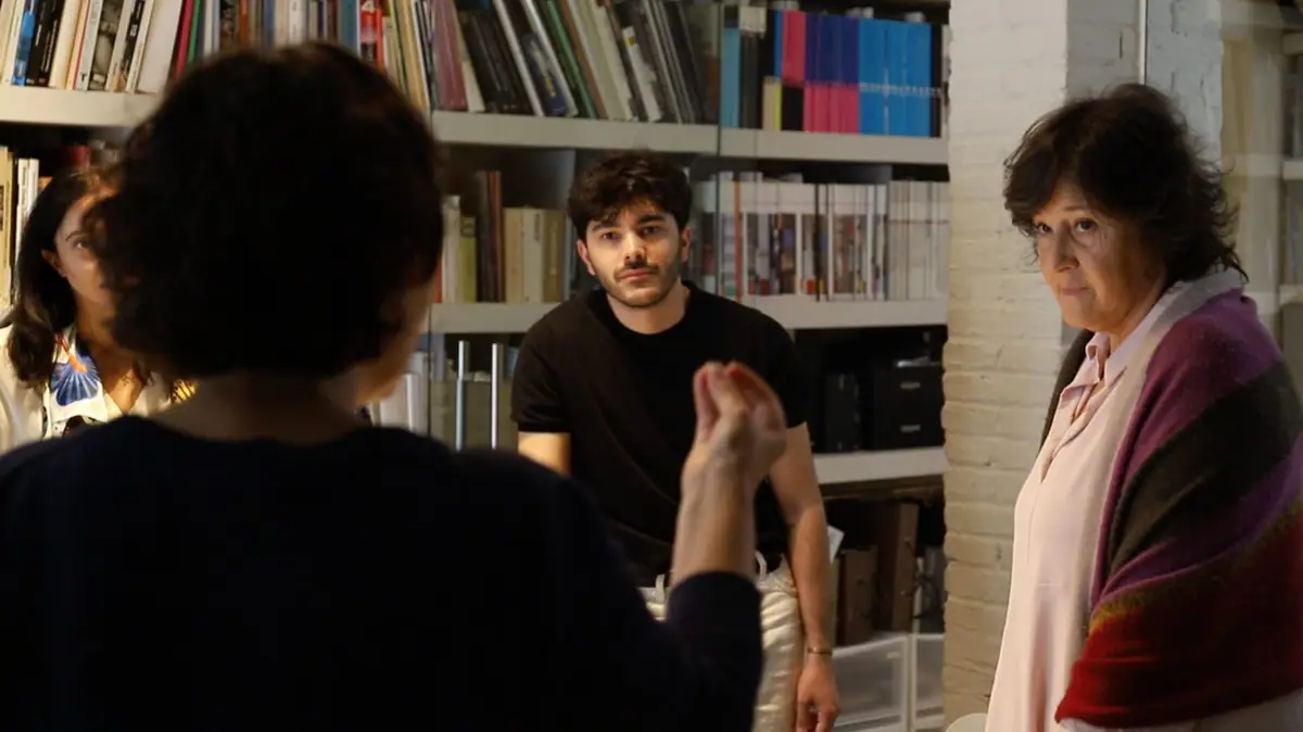 Isabel López Vilalta escucha a una compañera que explica algo al equipo, ante una estantería de libros