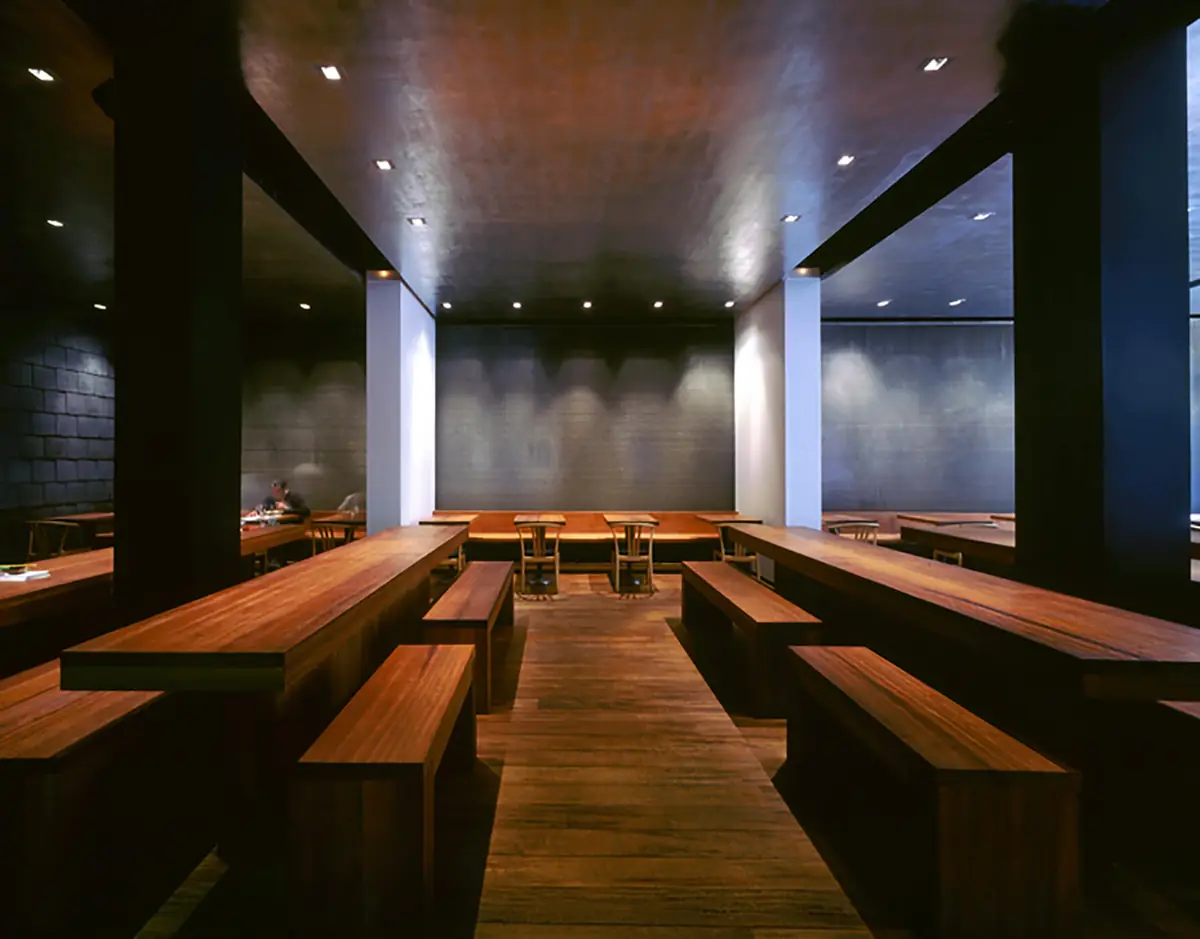 Sala de El Japonés con largas mesas y bancos de madera bajo un techo oscuro y paredes de piedra gris