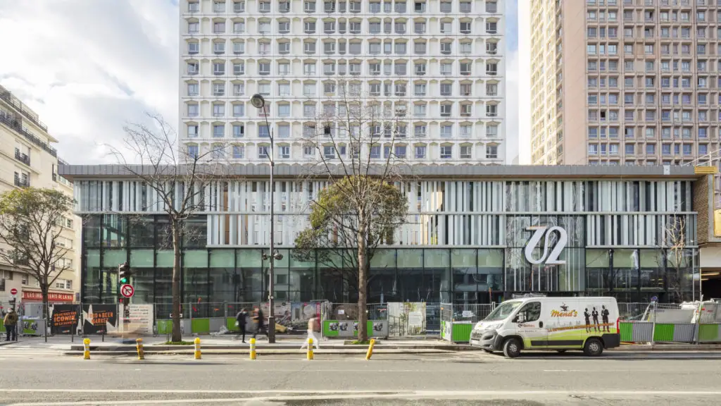 Fachada acristalada de Italik en l’Avenue d’Italie, con dos torres de viviendas detrás y vallas de obra en la acera