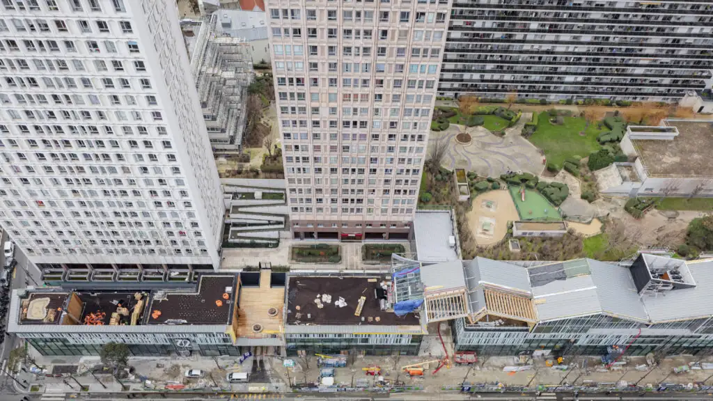 Vista aérea de Italik en obras: la cubierta del nuevo edificio junto a la avenida y, detrás, un jardín entre torres de viviendas