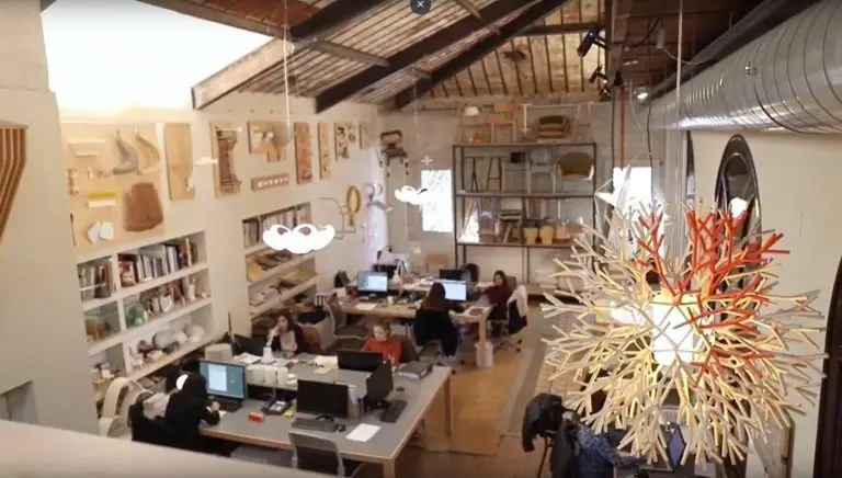 Vista desde el altillo del estudio de Lagranja Design, con mesas de trabajo, estanterías con piezas y una lámpara de varillas blancas y rojas en primer plano