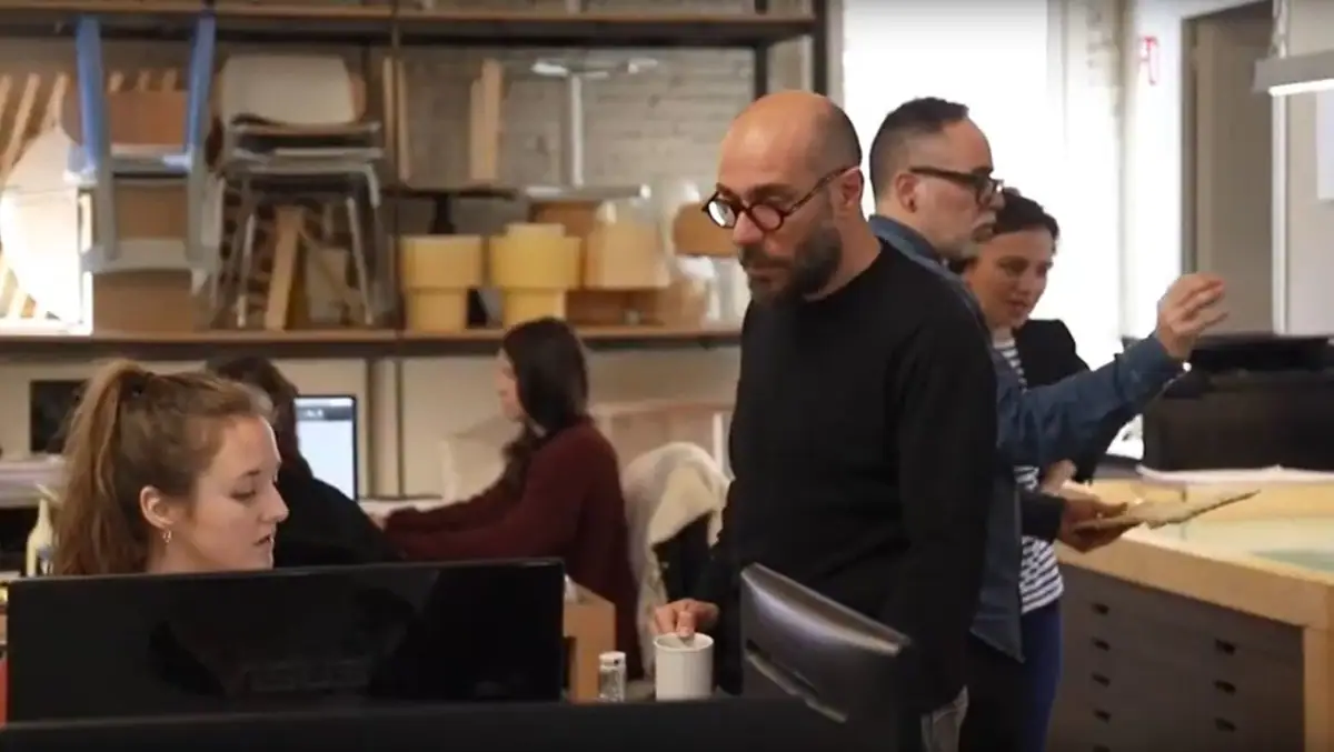 Varias personas del equipo de Lagranja Design comentan un proyecto junto a una mesa de planos, con estanterías de prototipos al fondo