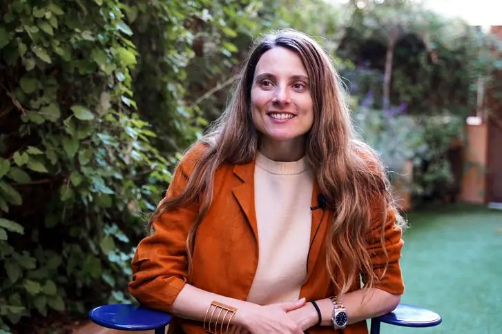 Retrato de Cristina Domínguez Lucas, con chaqueta naranja, sonriendo en un jardín