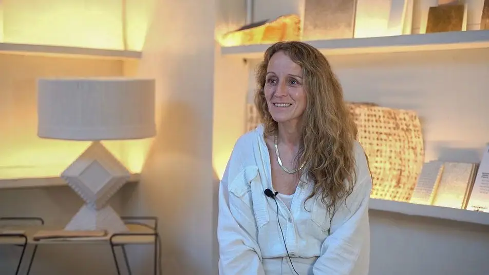 Naroa Quirós sonríe durante la entrevista, sentada ante unas baldas iluminadas con piezas de cerámica y una lámpara de mesa