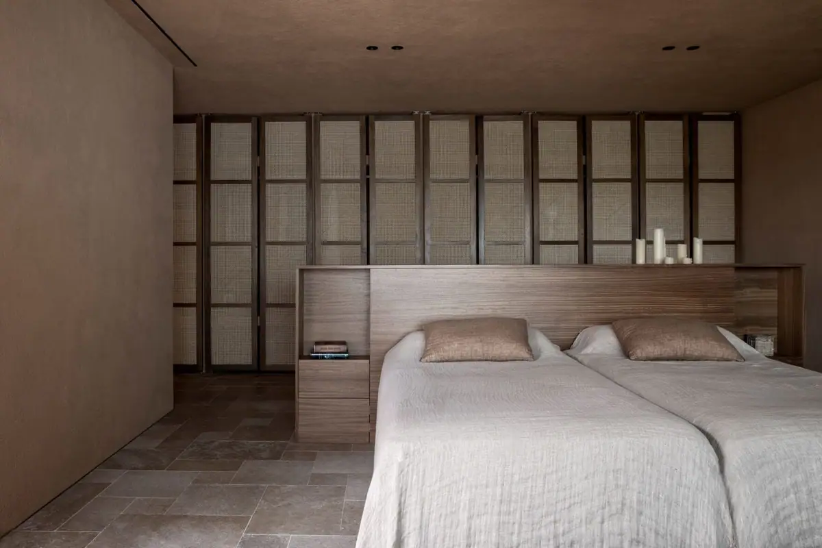 Dormitorio con dos camas, cabecero de madera y armarios de puertas de rejilla, con suelo de losas de piedra