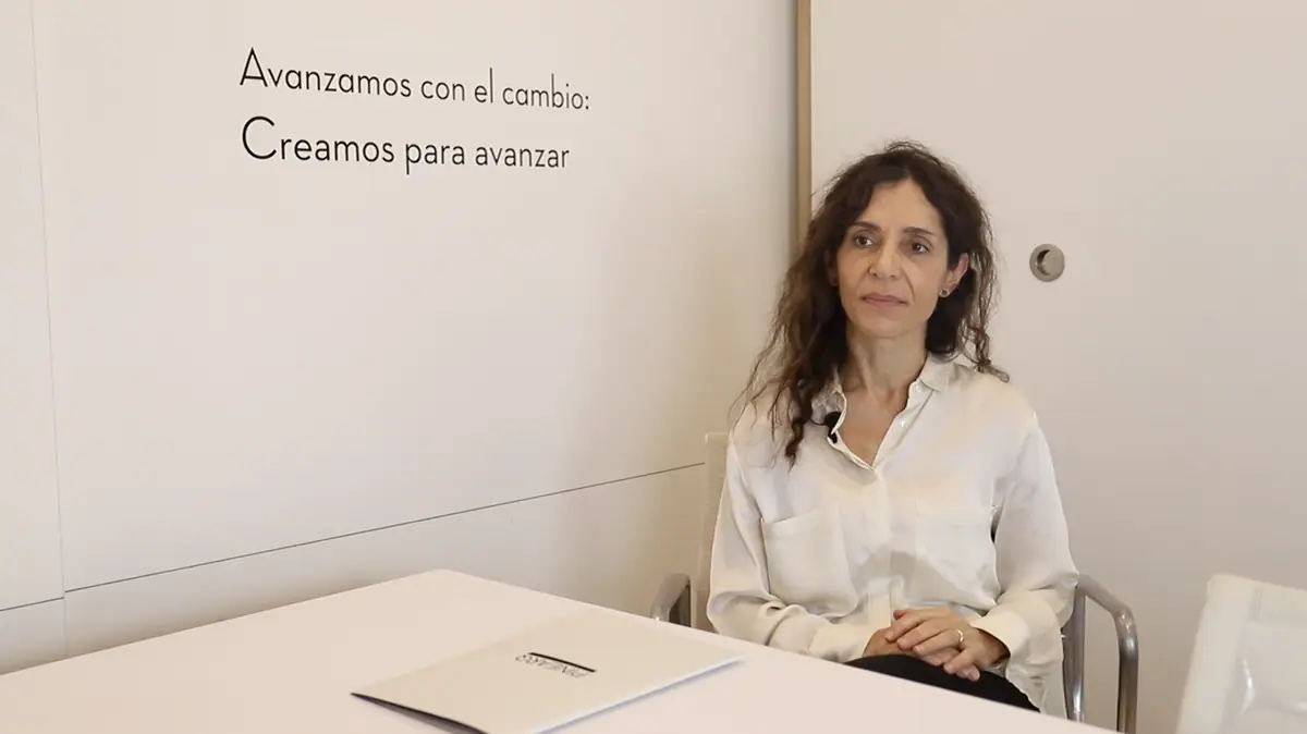 Inmaculada Casado sentada a una mesa blanca durante la entrevista, junto a un rótulo en la pared del estudio