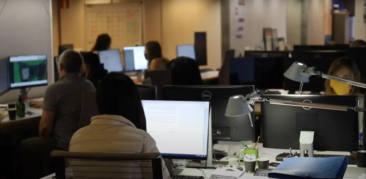 Equipo del estudio trabajando ante varias pantallas, con flexos y tableros de proyecto al fondo